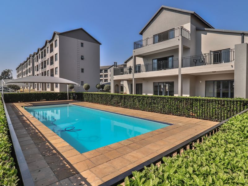 A well-maintained communal swimming pool area featuring paved decking, metal safety fencing, and views of the apartment complex buildings.