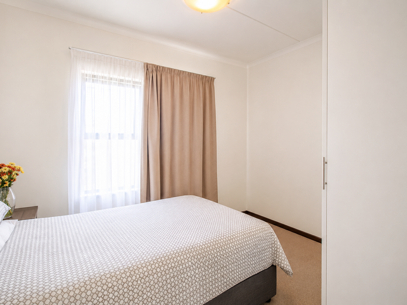 A clean and well-maintained bedroom featuring neutral walls, carpeted flooring, and a built-in wardrobe, offering a bright and comfortable living space.