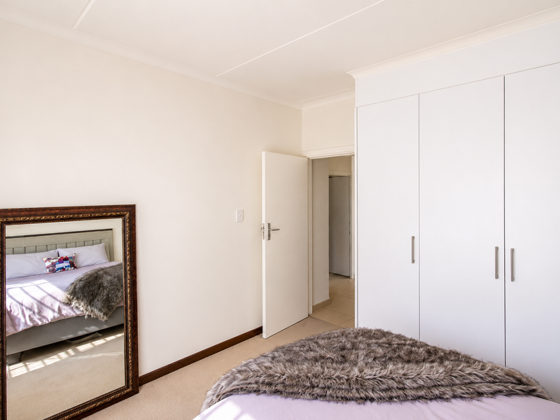 A well-maintained bedroom featuring neutral walls, carpeted flooring, and ample built-in cupboard storage with a clean, minimalist aesthetic.