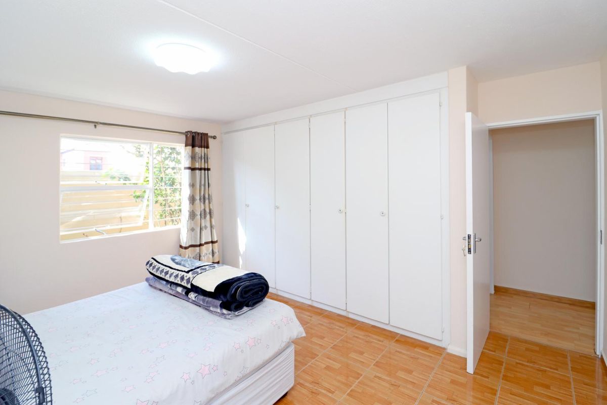 A bedroom featuring built-in floor-to-ceiling cupboards, tiled flooring, and a window providing natural light.