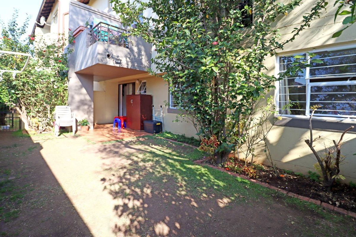 A rear exterior view of the townhouse featuring a small patio area, garden space, and a balcony above.