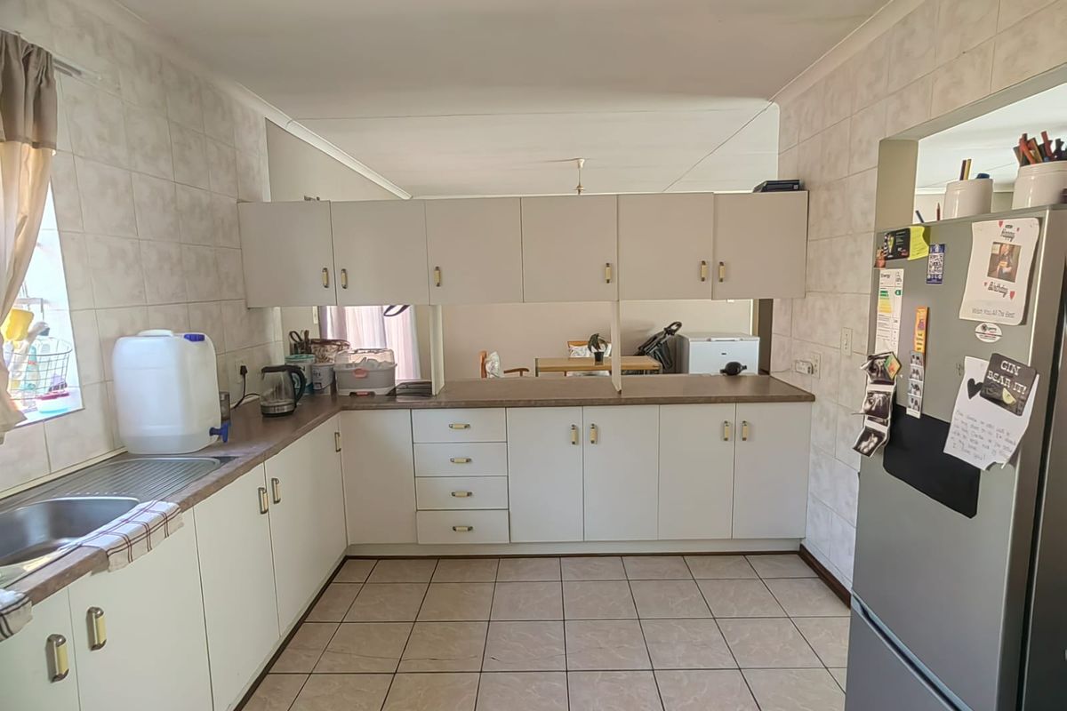 A functional kitchen featuring white cabinetry, laminate countertops, tiled splashbacks, and tiled flooring, offering a practical layout with a breakfast bar opening to the living area.