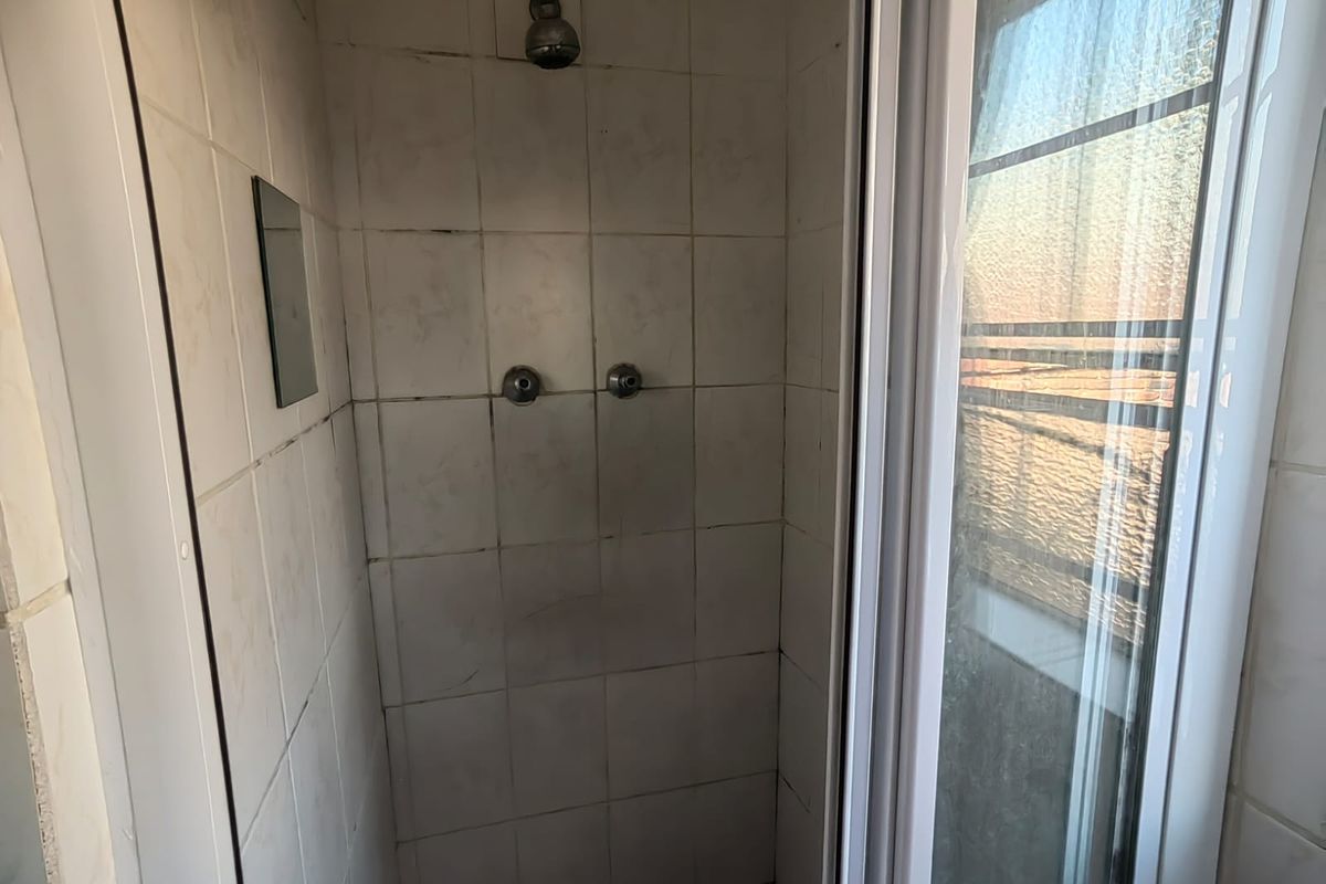 A compact shower enclosure featuring white wall tiles, a fixed shower head, and a sliding glass door.