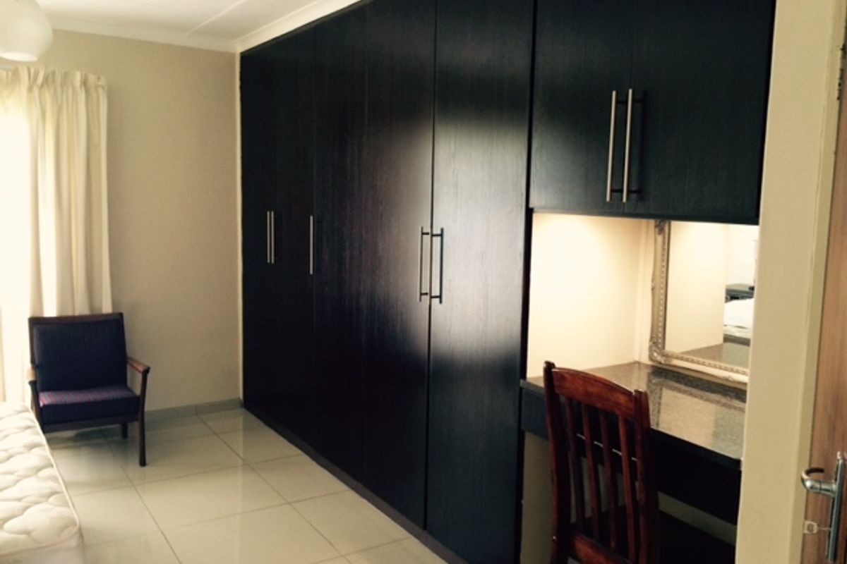 A bedroom featuring extensive dark wood built-in cabinetry with integrated vanity and polished tile flooring.