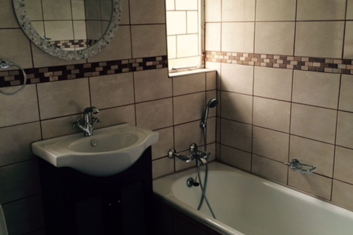 A functional bathroom featuring a built-in bathtub with shower mixer, a vanity basin, and tiled walls with a decorative border.