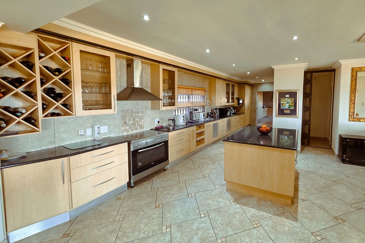 Spacious kitchen featuring light wood cabinetry, granite countertops, a central island, and integrated stainless steel appliances with tiled flooring throughout.