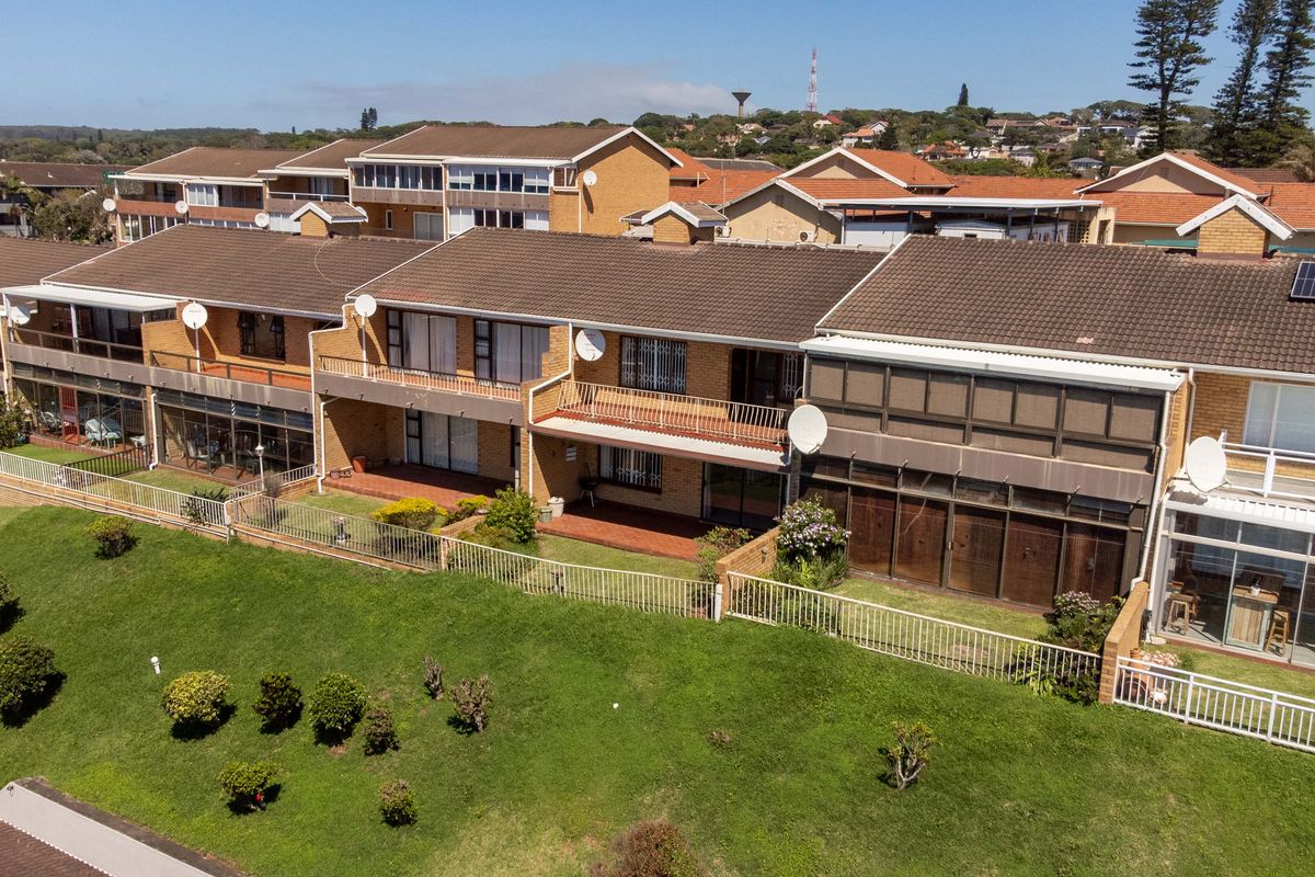 Aerial view of a townhouse complex featuring brick facades, tiled roofs, private balconies, and ground-floor patios overlooking a shared lawn area.