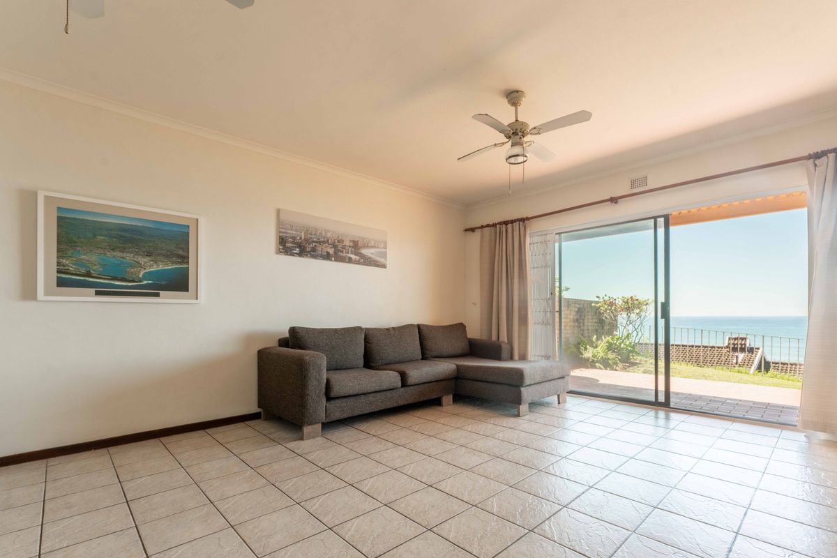 Bright living room featuring ceramic floor tiles, a ceiling fan, and large sliding glass doors opening to a patio with ocean views.