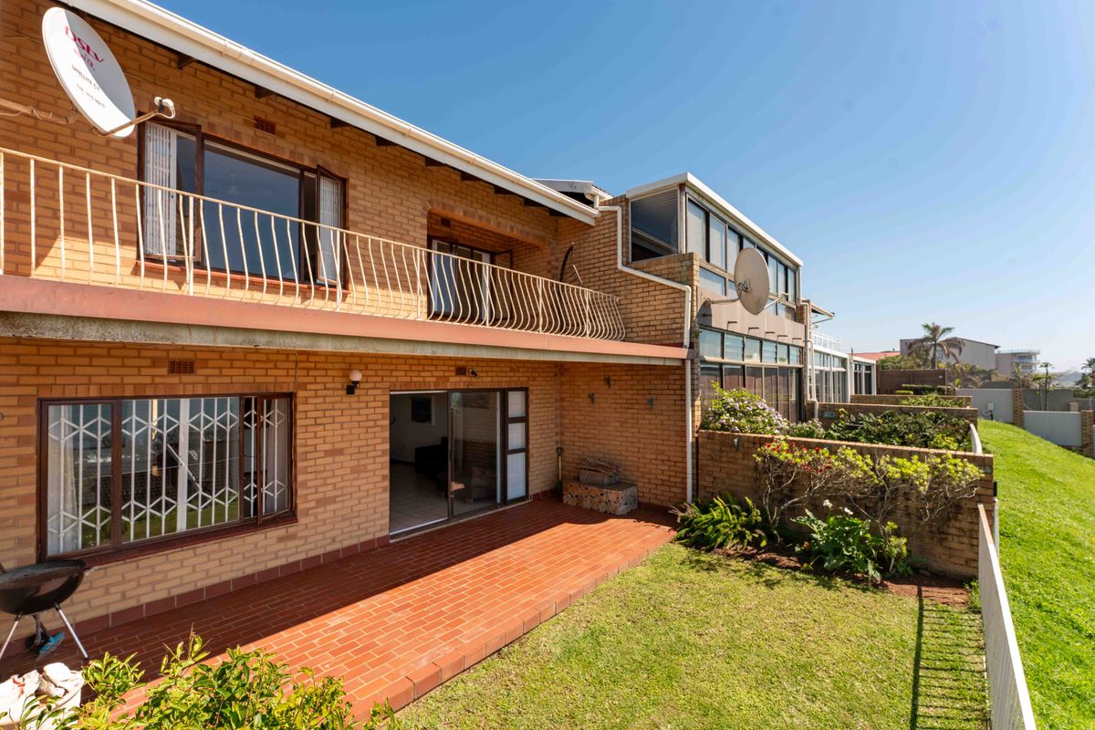 Rear view of a brick townhouse featuring a terracotta tiled patio, upper-level balcony with metal railing, and a small private garden area.