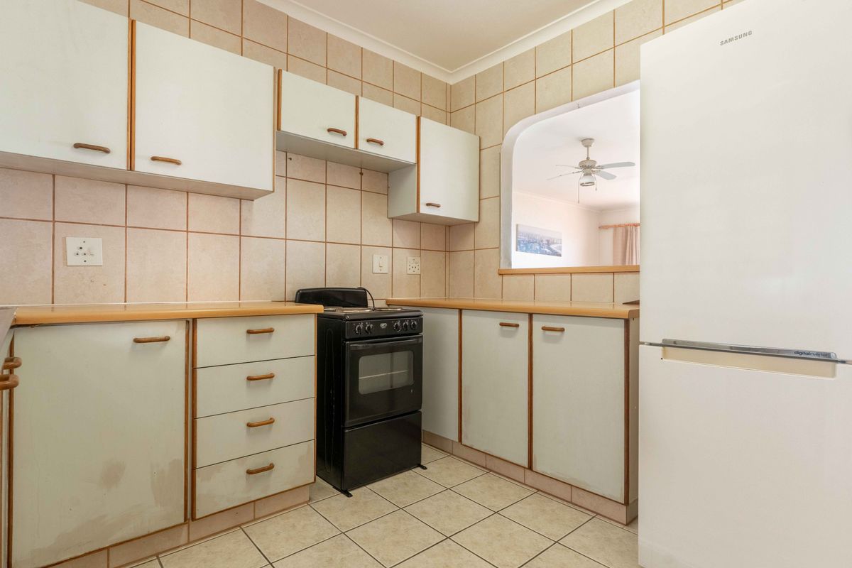 A functional kitchen featuring tiled splashbacks, laminate countertops, built-in cabinetry, and a pass-through window connecting to the adjacent living area.