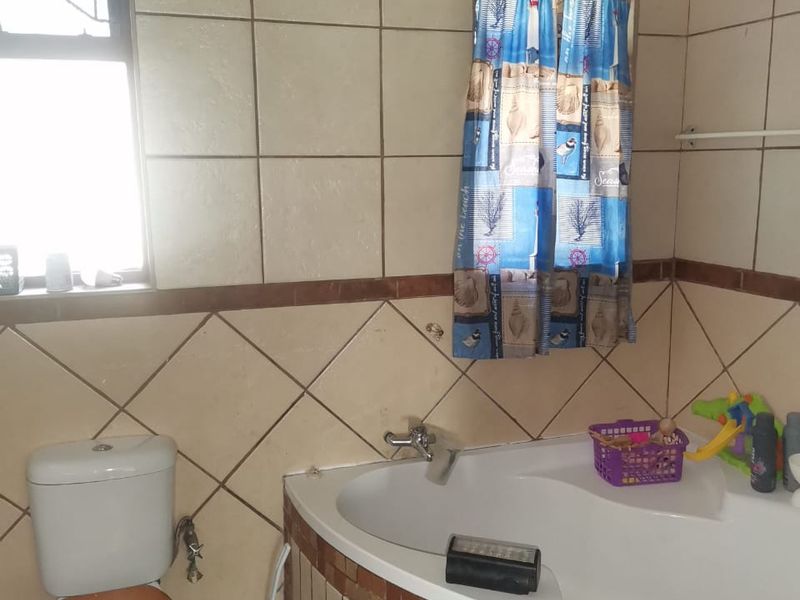 A dated bathroom featuring a corner bathtub, ceramic wall tiling, and a standard toilet, requiring cosmetic updates to improve its overall condition and appeal.