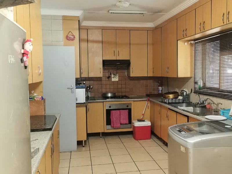 A functional kitchen featuring wood-tone cabinetry, built-in oven and hob, tiled flooring, and ample storage space, offering potential for a modern renovation.