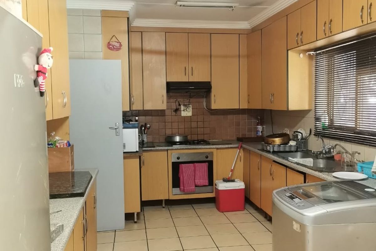 A functional kitchen featuring wood-tone cabinetry, built-in oven and hob, tiled flooring, and ample storage space, offering potential for a modern renovation.