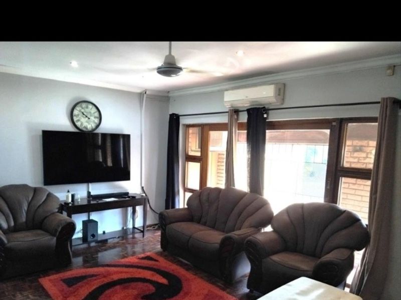 A living room featuring parquet flooring, a ceiling fan, and a wall-mounted air conditioning unit with access to the exterior through sliding glass doors.