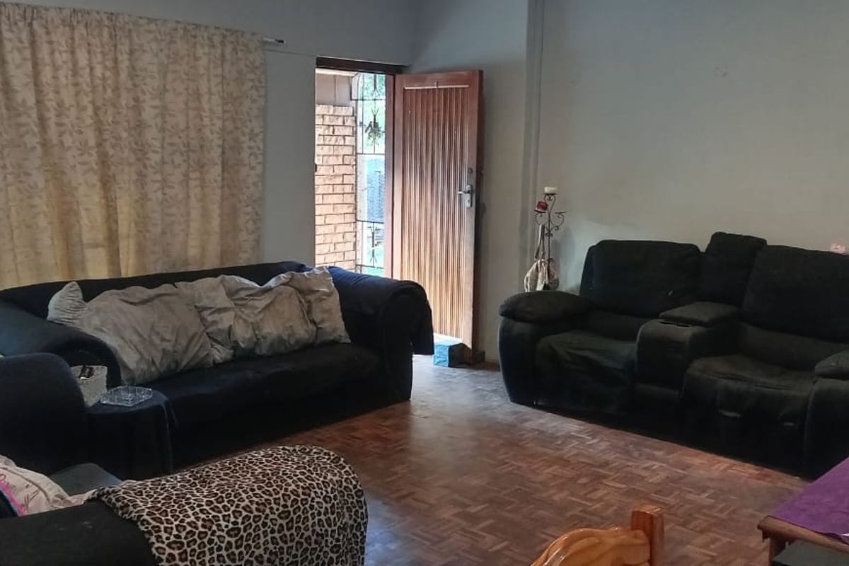A living room featuring classic parquet flooring, natural light from a sliding glass door, and direct access to the exterior via a timber door.