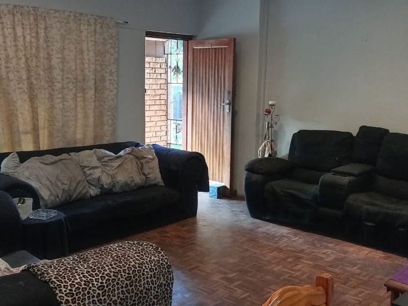 A living room featuring classic parquet flooring, natural light from a sliding glass door, and direct access to the exterior via a timber door.