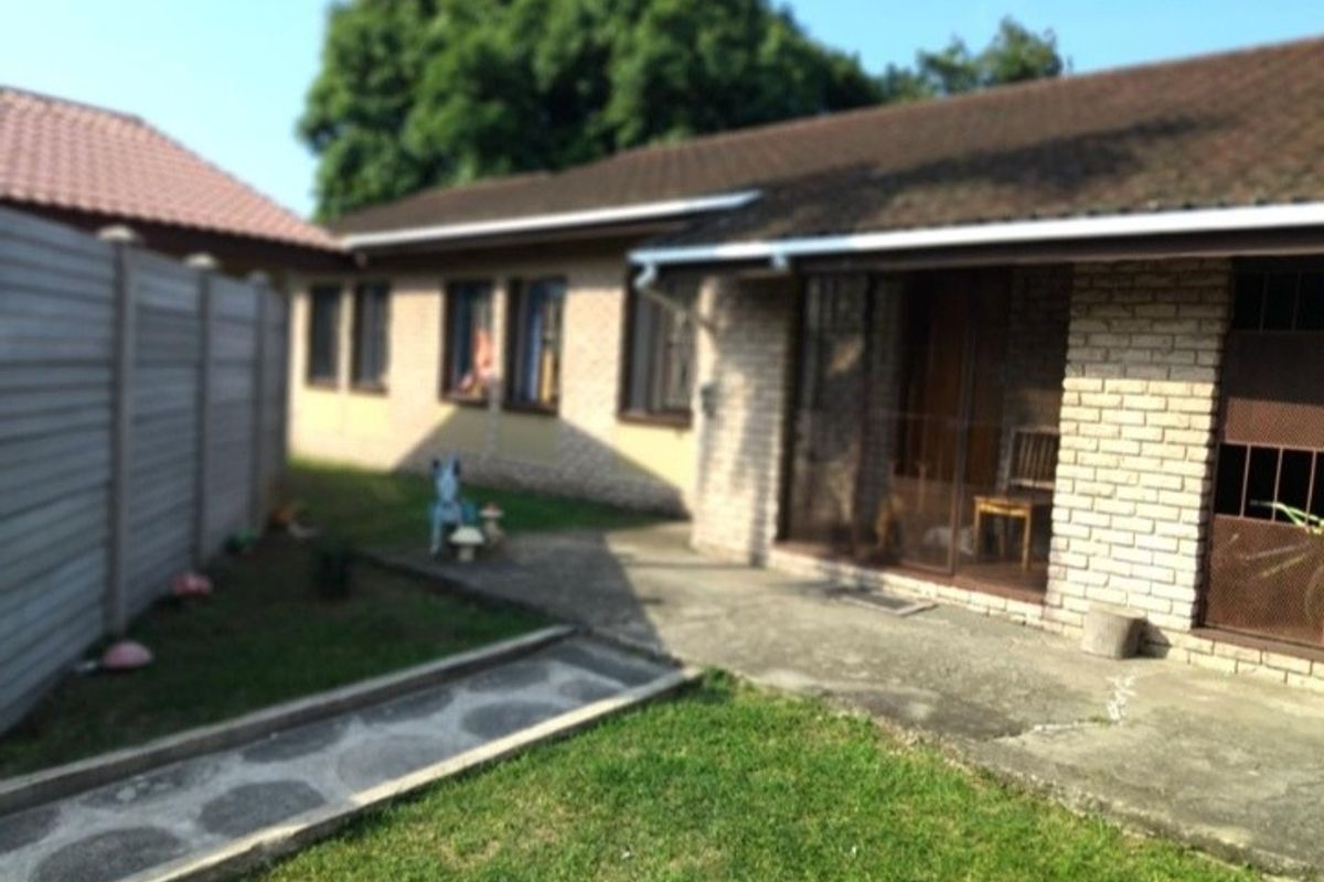 Rear view of the property featuring a brick facade, tiled roof, and a concrete patio area adjacent to a small garden and boundary wall.