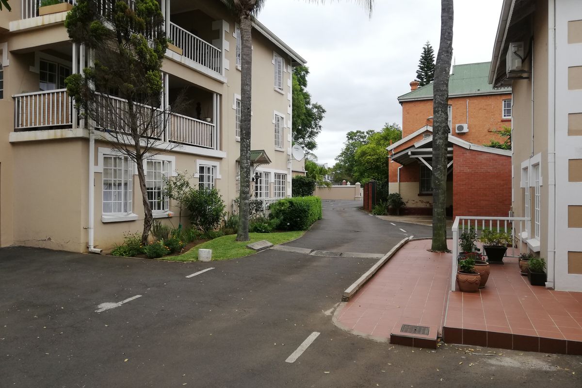 Exterior view of the apartment complex featuring an asphalt driveway, tiled patio area, and multi-level balconies with white railings.