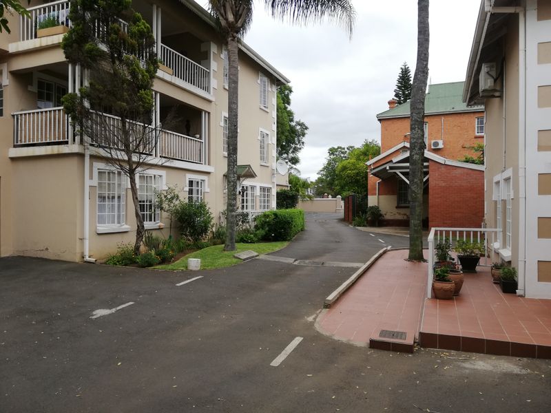 Exterior view of the apartment complex featuring an asphalt driveway, tiled patio area, and multi-level balconies with white railings.