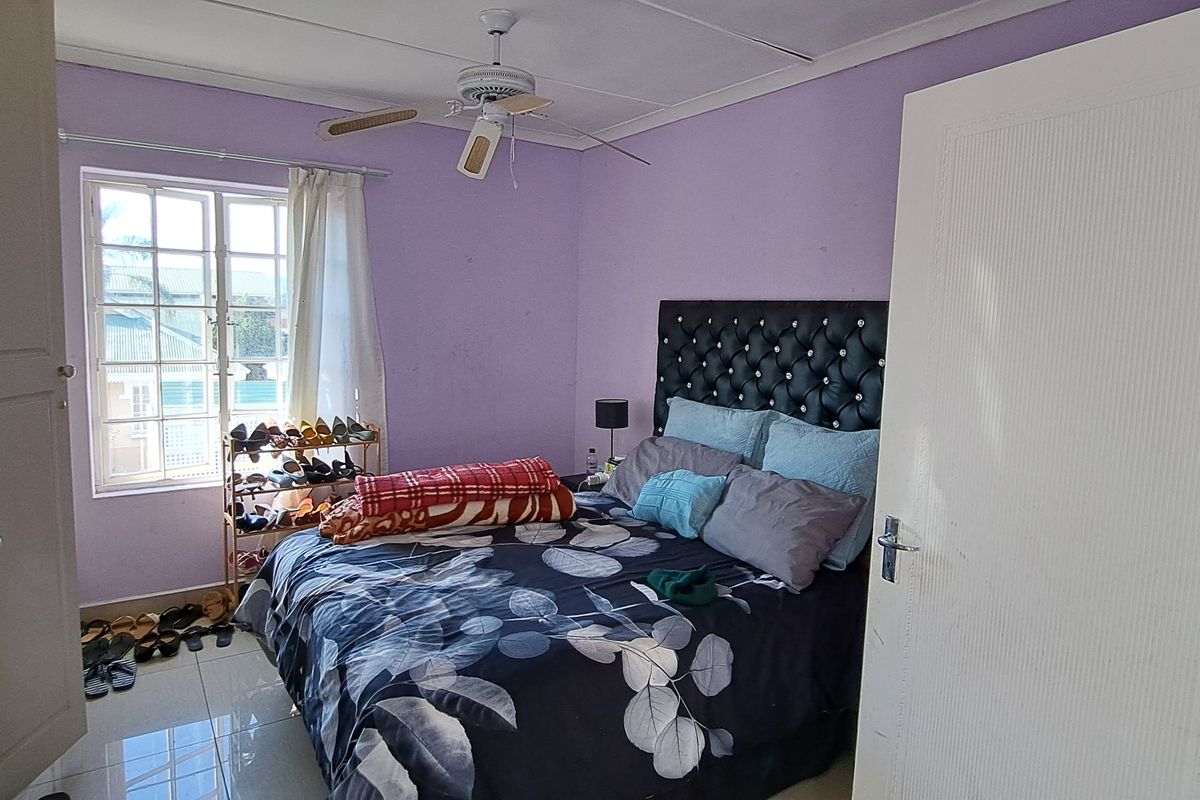 A bedroom featuring tiled flooring, a ceiling fan, and a window, currently requiring cosmetic updates to the wall finishes.