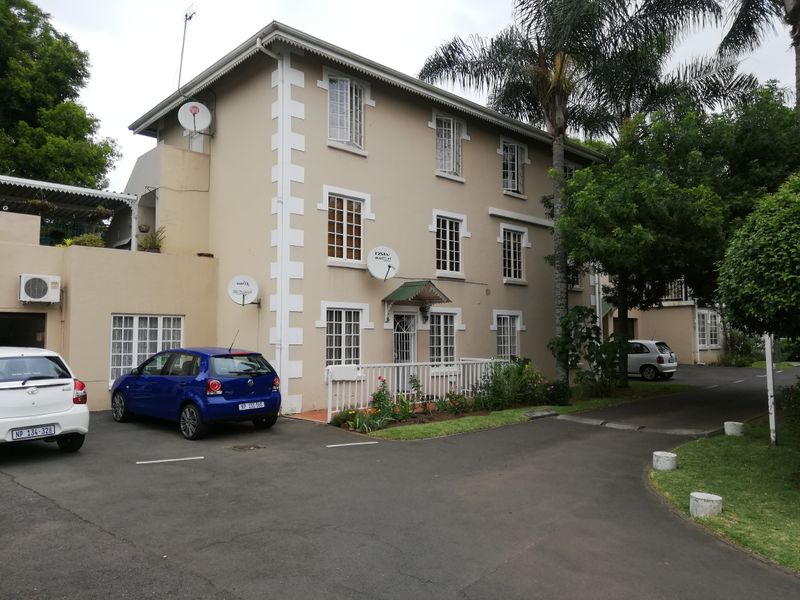 Exterior view of a multi-story apartment building featuring a paved driveway, white picket fencing, and established landscaping.