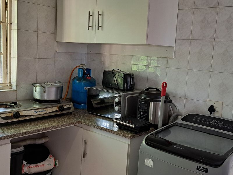 A functional kitchen area featuring built-in cabinetry, a stainless steel sink, and tiled backsplash, offering potential for modernization and improved layout.