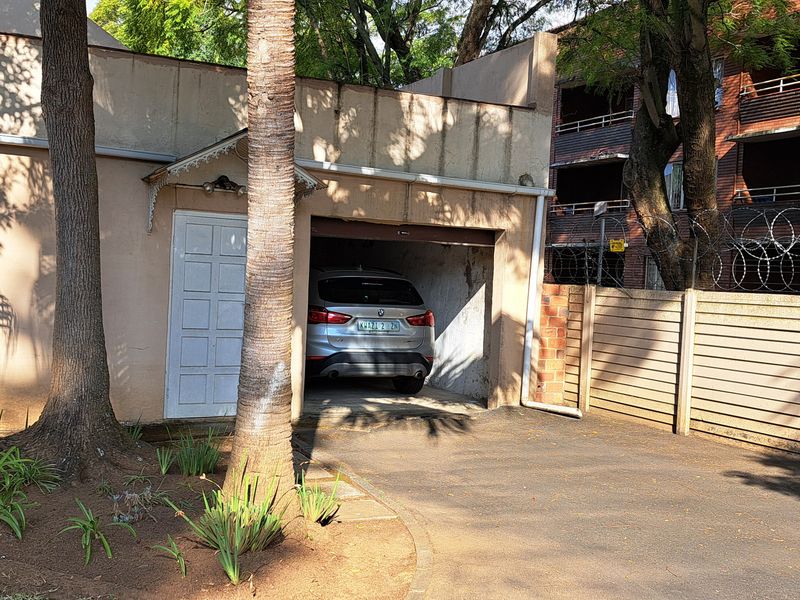 Exterior view of a residential garage with a paved driveway and perimeter security fencing.