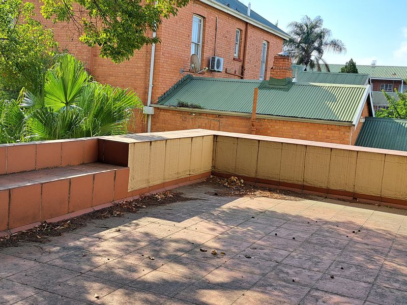 An open-air balcony featuring built-in tiled bench seating and tiled flooring, offering a functional outdoor space with potential for revitalization.