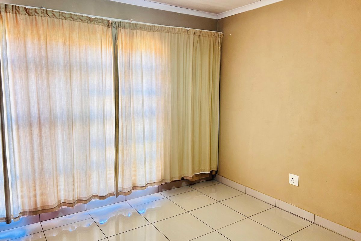 An empty bedroom featuring neutral tiled flooring and large windows with existing curtain tracks, ready for personalization.