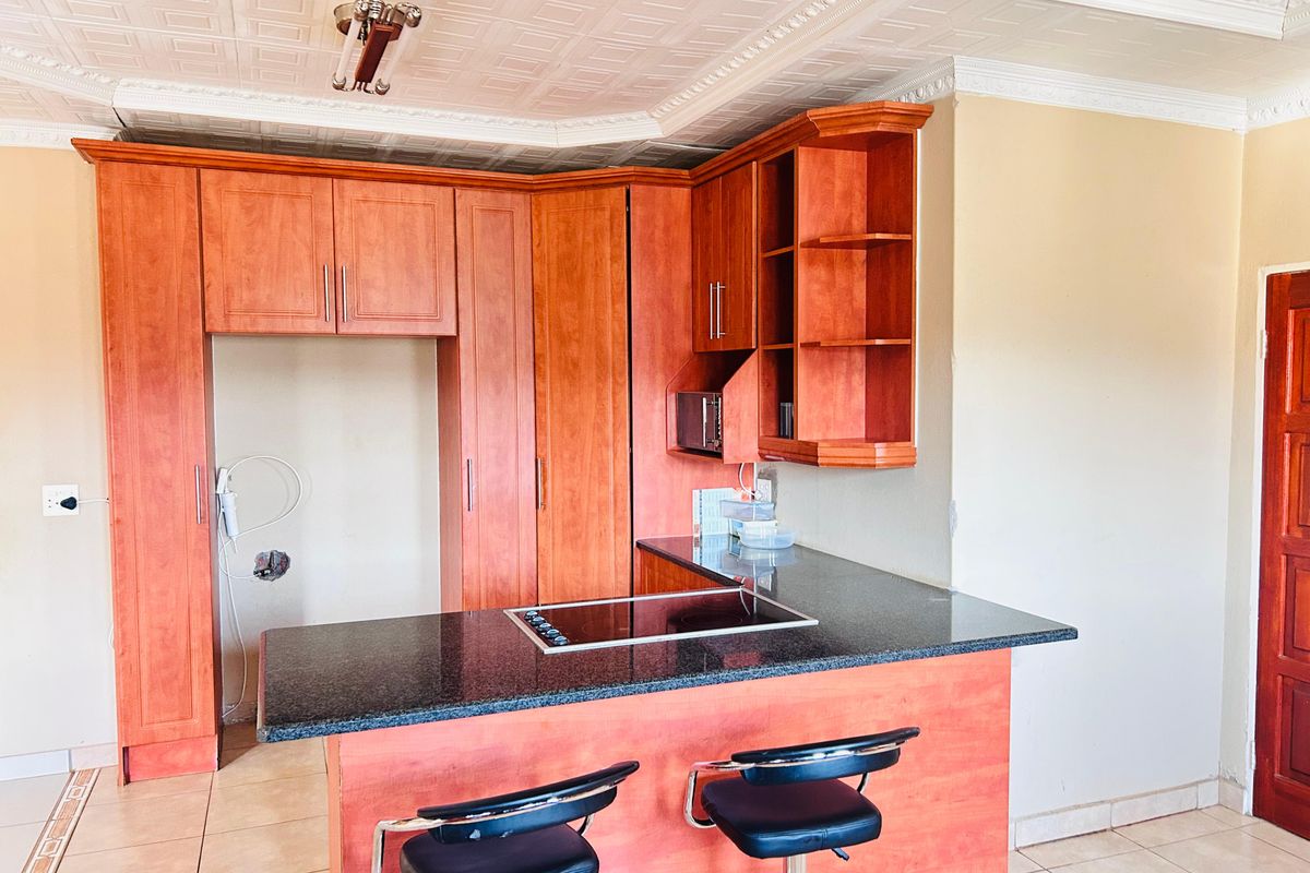 A kitchen area featuring wooden cabinetry, a granite countertop with an integrated electric hob, and decorative ceiling tiles.