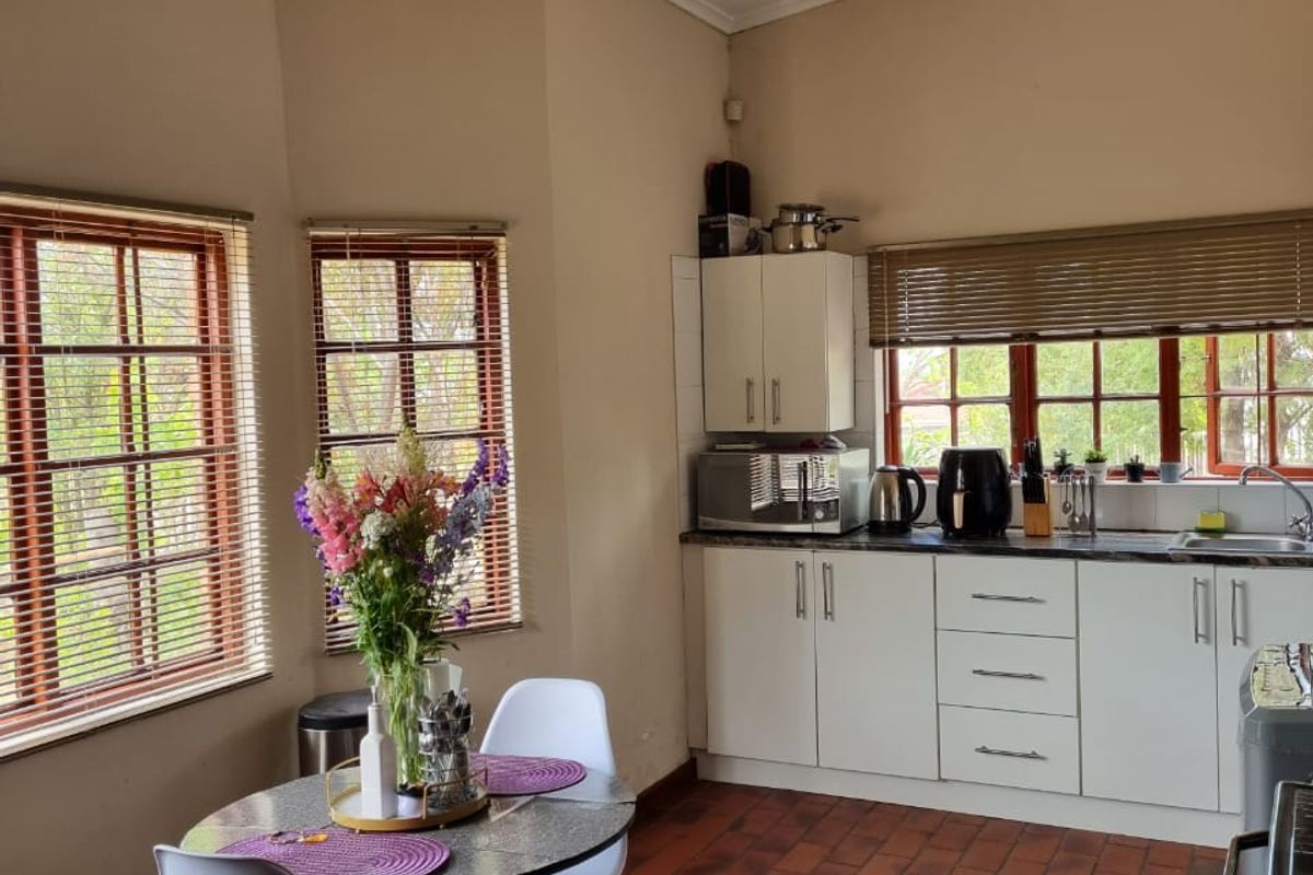 A functional kitchen featuring built-in cabinetry, laminate countertops, a stainless steel sink, and classic terracotta tile flooring with natural light from multiple windows.