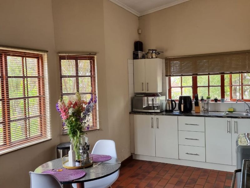 A functional kitchen featuring built-in cabinetry, laminate countertops, a stainless steel sink, and classic terracotta tile flooring with natural light from multiple windows.
