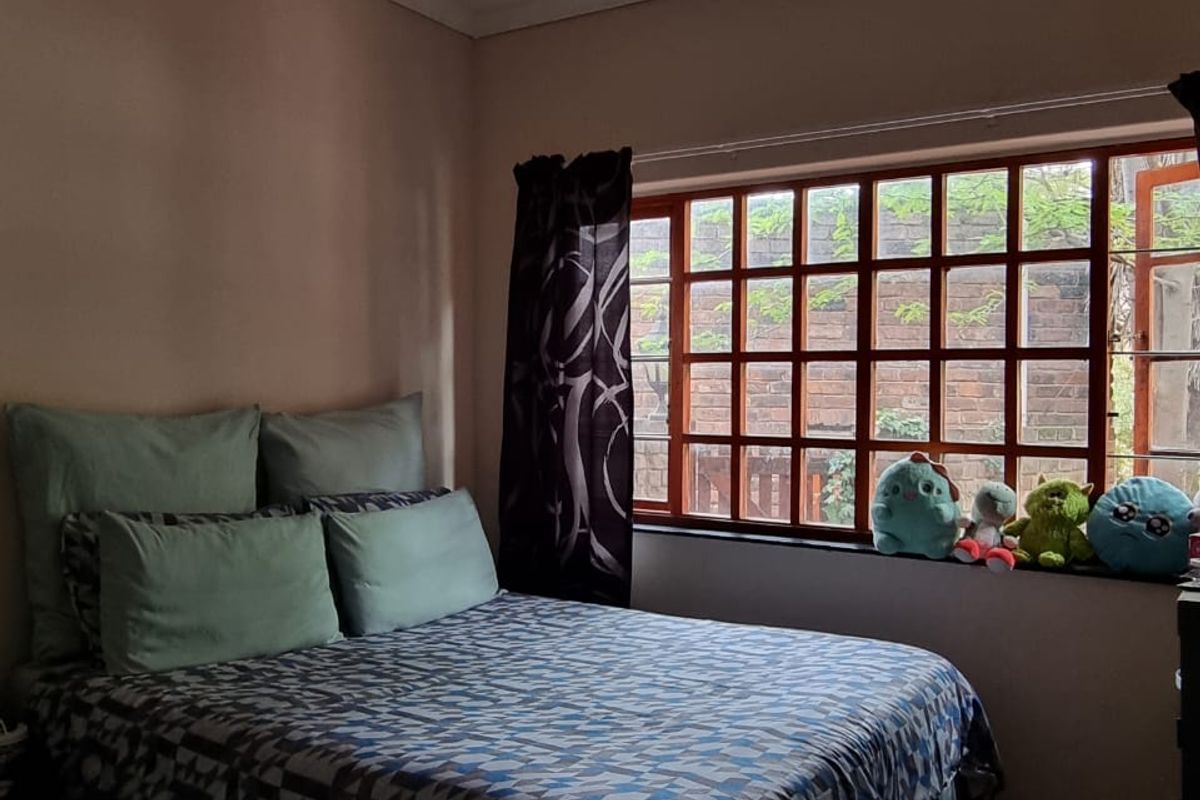 A bedroom featuring terracotta tile flooring and a large grid-pattern window that allows natural light into the space.