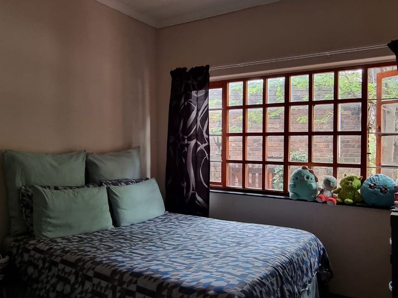 A bedroom featuring terracotta tile flooring and a large grid-pattern window that allows natural light into the space.