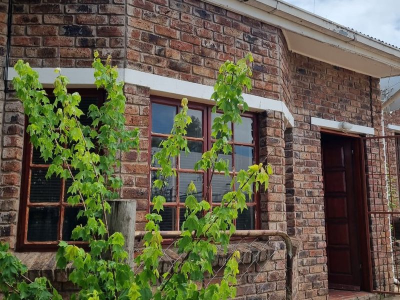 A view of the front facade featuring face brick construction, timber framed windows, and a timber entrance door with a concrete pathway.