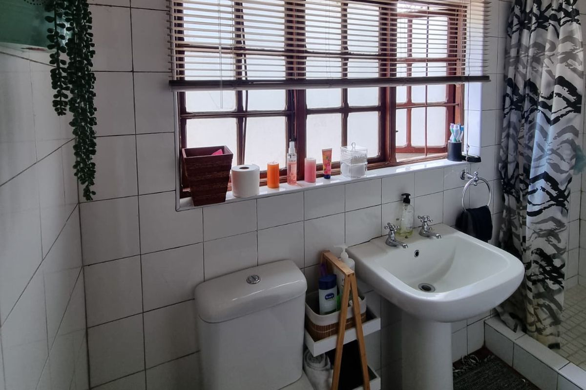 A functional bathroom featuring a pedestal basin, toilet, and shower area with tiled walls and a window providing natural light.