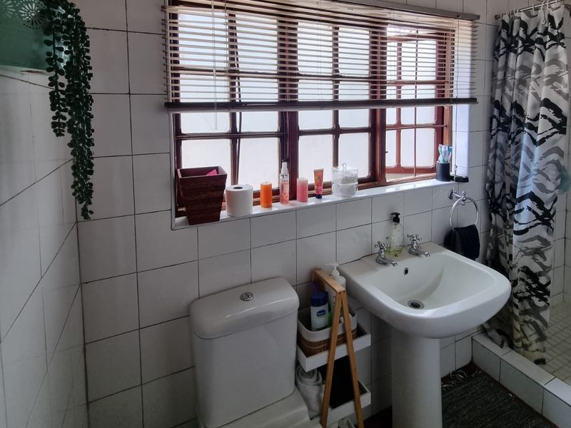 A functional bathroom featuring a pedestal basin, toilet, and shower area with tiled walls and a window providing natural light.