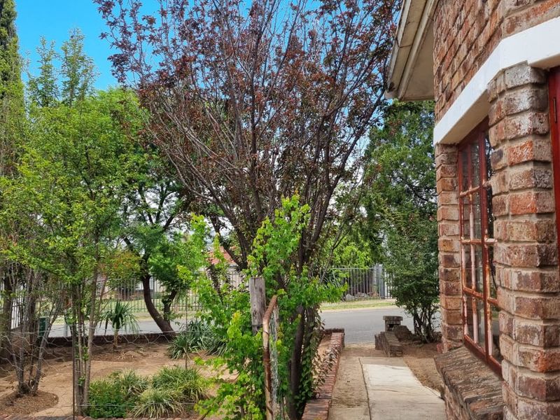 A view of the front exterior featuring a face brick facade, concrete pathway, and established garden area with mature trees.