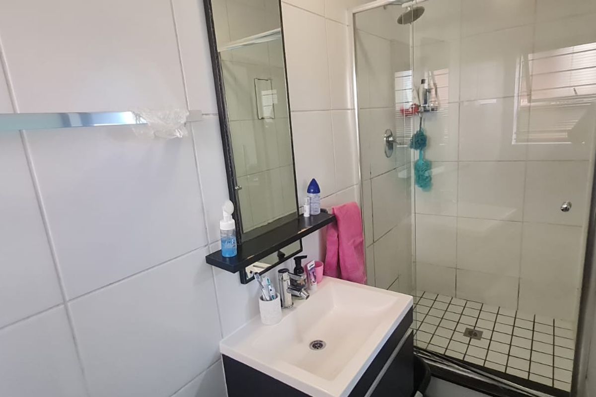A functional bathroom featuring a shower enclosure with tiled walls and a modern vanity basin with an integrated mirror.