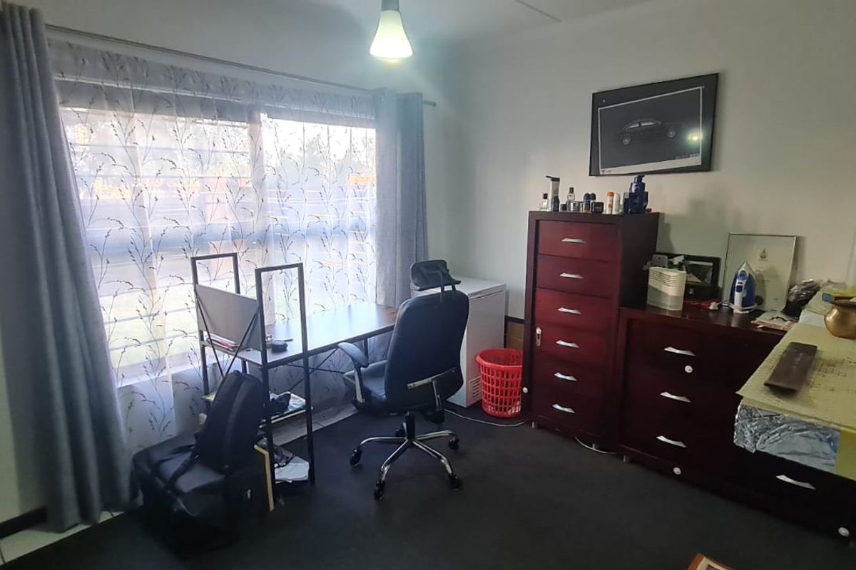 A functional bedroom space featuring a large window with curtain rails, suitable for use as a bedroom or home office.