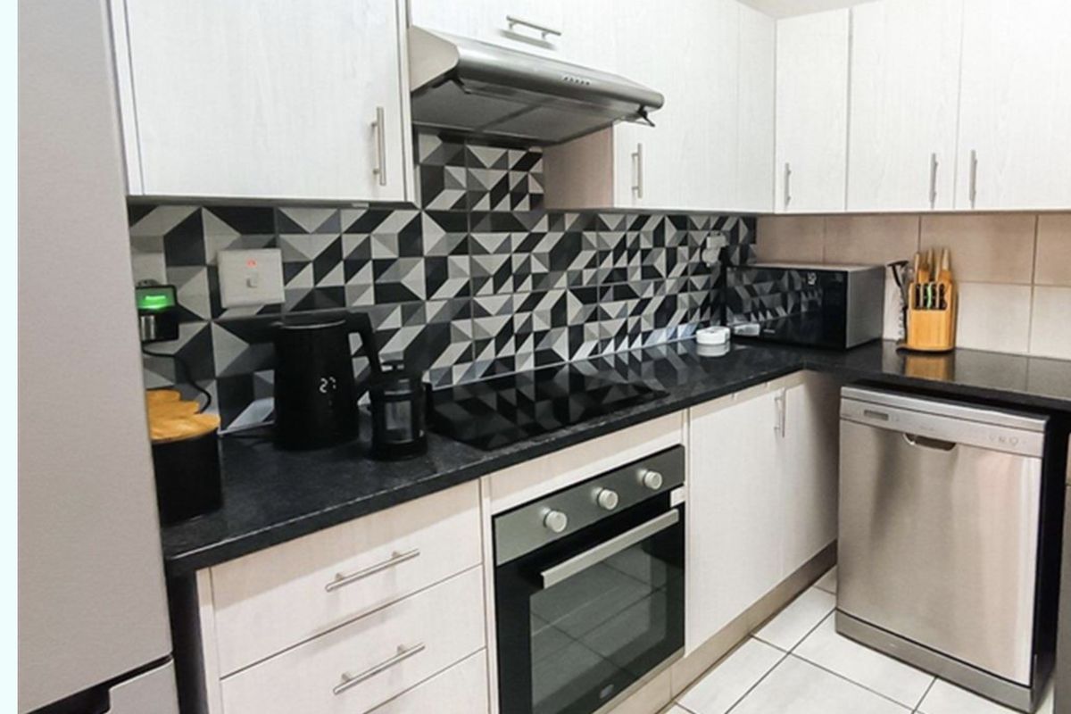 Modern kitchen featuring white cabinetry, black stone countertops, a geometric tiled splashback, and integrated stainless steel appliances.