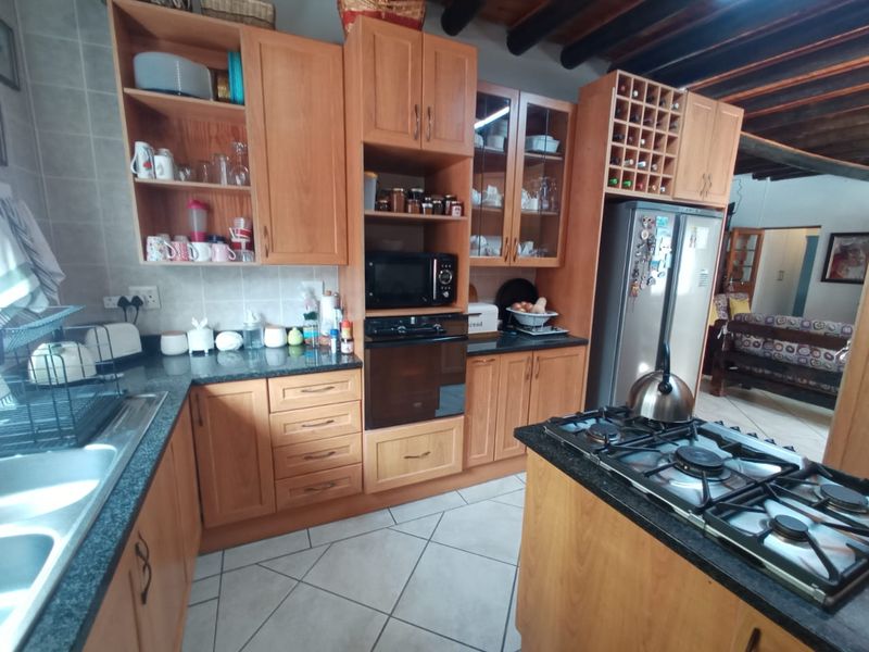 A functional kitchen featuring wooden cabinetry, granite countertops, a gas hob, built-in oven, and exposed timber ceiling beams, offering a warm, traditional aesthetic.