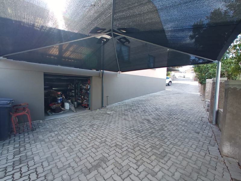Exterior view of a paved driveway area featuring a large shade sail structure and access to a garage space.
