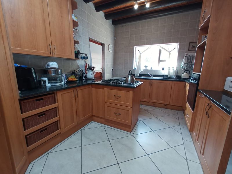 A functional kitchen featuring wooden cabinetry, granite countertops, a gas hob, built-in oven, and exposed timber ceiling beams with tiled flooring.