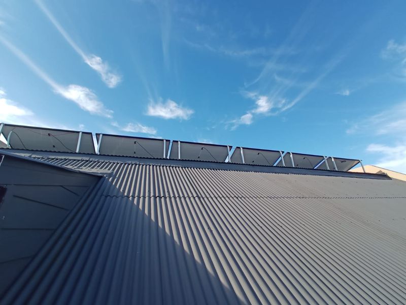 A view of the property's corrugated metal roof featuring a mounted solar panel array under a clear blue sky.