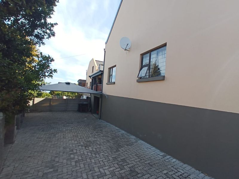 Side view of the duet property featuring a paved driveway, boundary wall, and exterior wall finishes with installed satellite dish.