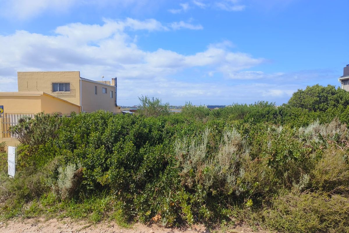 A view of a vacant residential plot featuring native vegetation and access to an unpaved road, adjacent to existing residential property.
