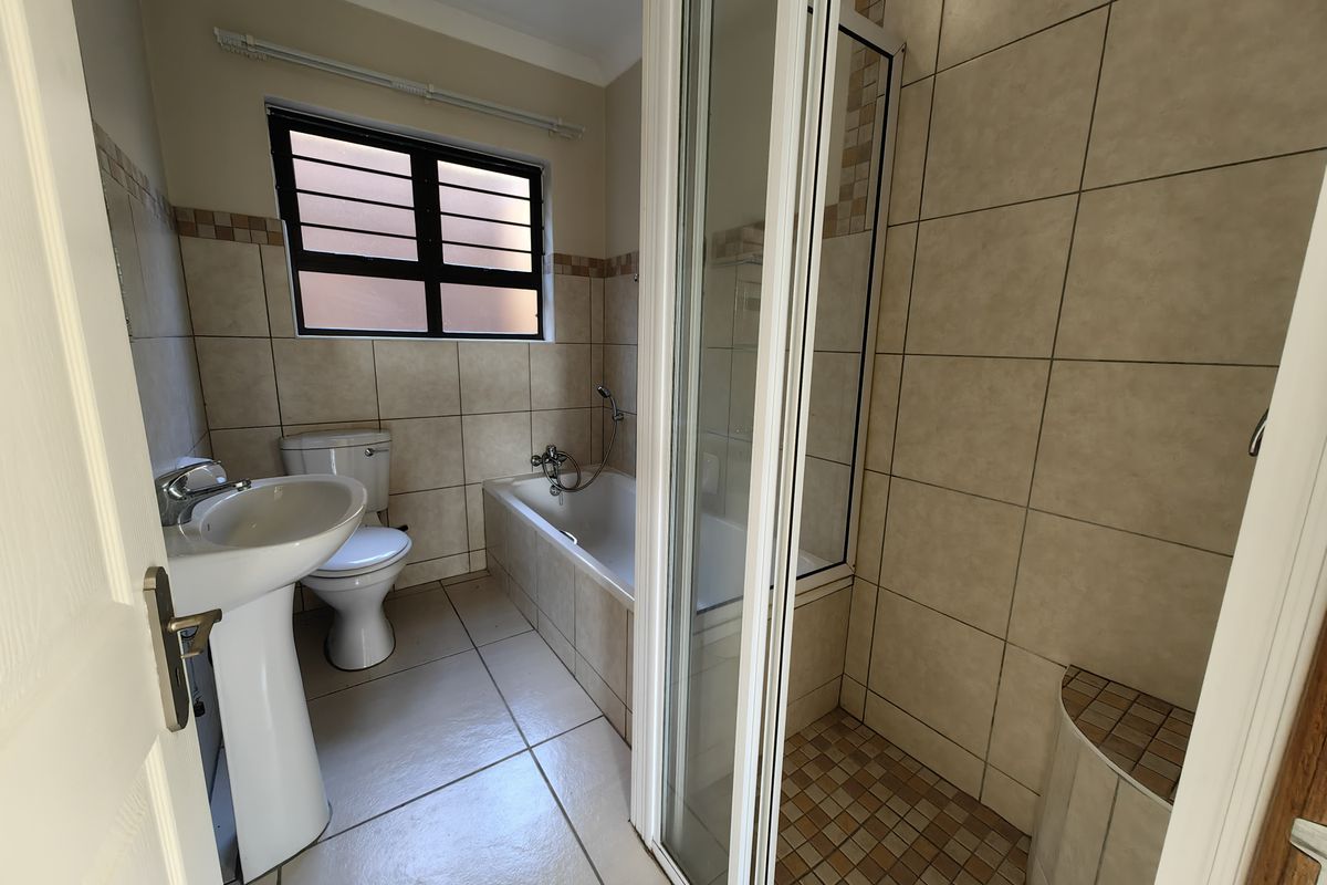 A functional bathroom featuring a pedestal basin, toilet, built-in bathtub, and a separate shower enclosure with tiled finishes throughout.