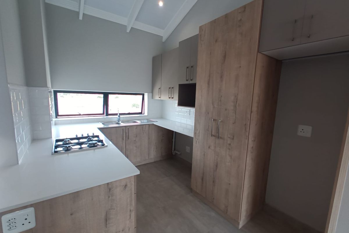 Modern kitchen featuring wood-grain cabinetry, white stone countertops, a built-in gas hob, and a vaulted ceiling with recessed lighting.