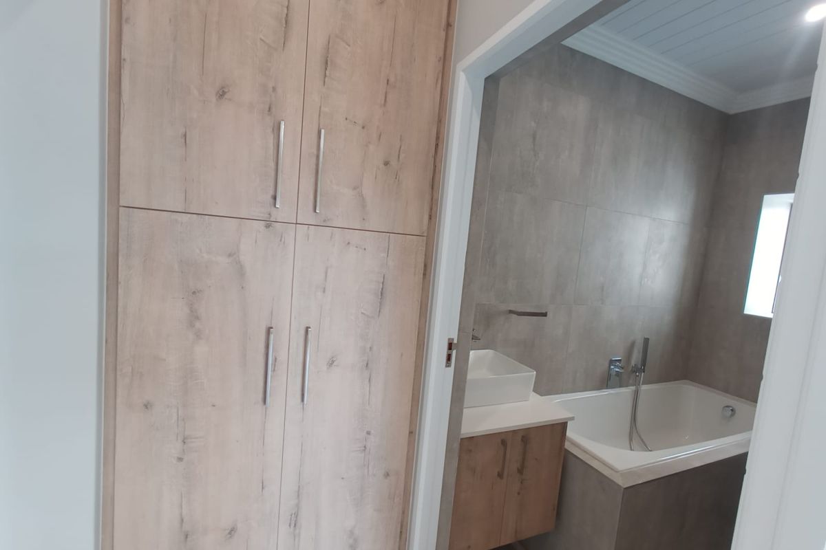 A modern bathroom featuring a built-in bathtub, a vessel sink vanity with wood-look cabinetry, and floor-to-ceiling storage cupboards in a matching finish.